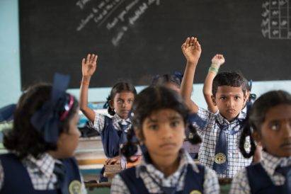 School children inside classroom raising their hands